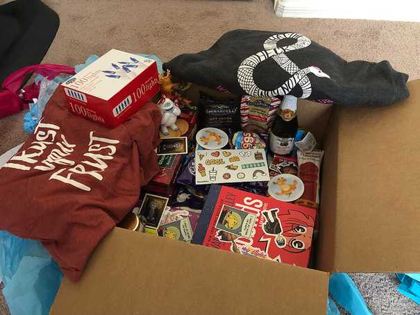 cardboard box filled with goodies like books, snacks, tshirts, and holiday lights.